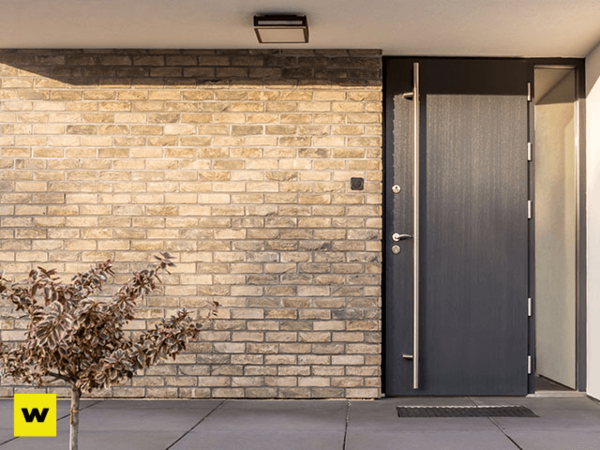 Moderne Haustür aus dunklem Metall neben heller Klinkerfassade, minimalistisches Design.