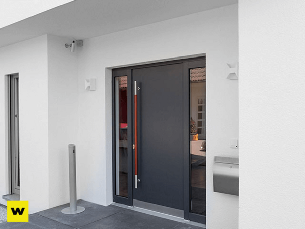 Moderne Haustür aus dunklem Aluminium mit Seitenteil an einem weißen, minimalistischen Haus.