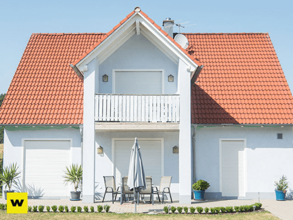 Modernes Einfamilienhaus mit rotem Dach, Balkon, Terrasse und geschlossenen Rollläden.